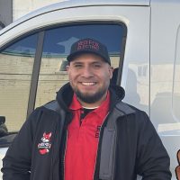 Hector, Red Fox Electric Service Technician, Smiling In Branded Jacket And Hat Beside Service Van In Denver, CO.